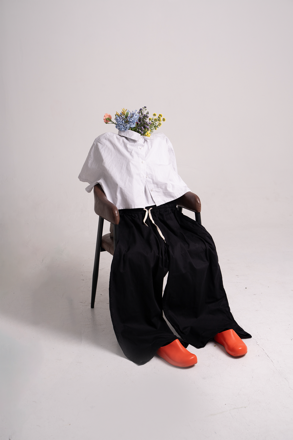 A white shirt, black pants, and orange shoes posed on a chair with flowers in the collar.