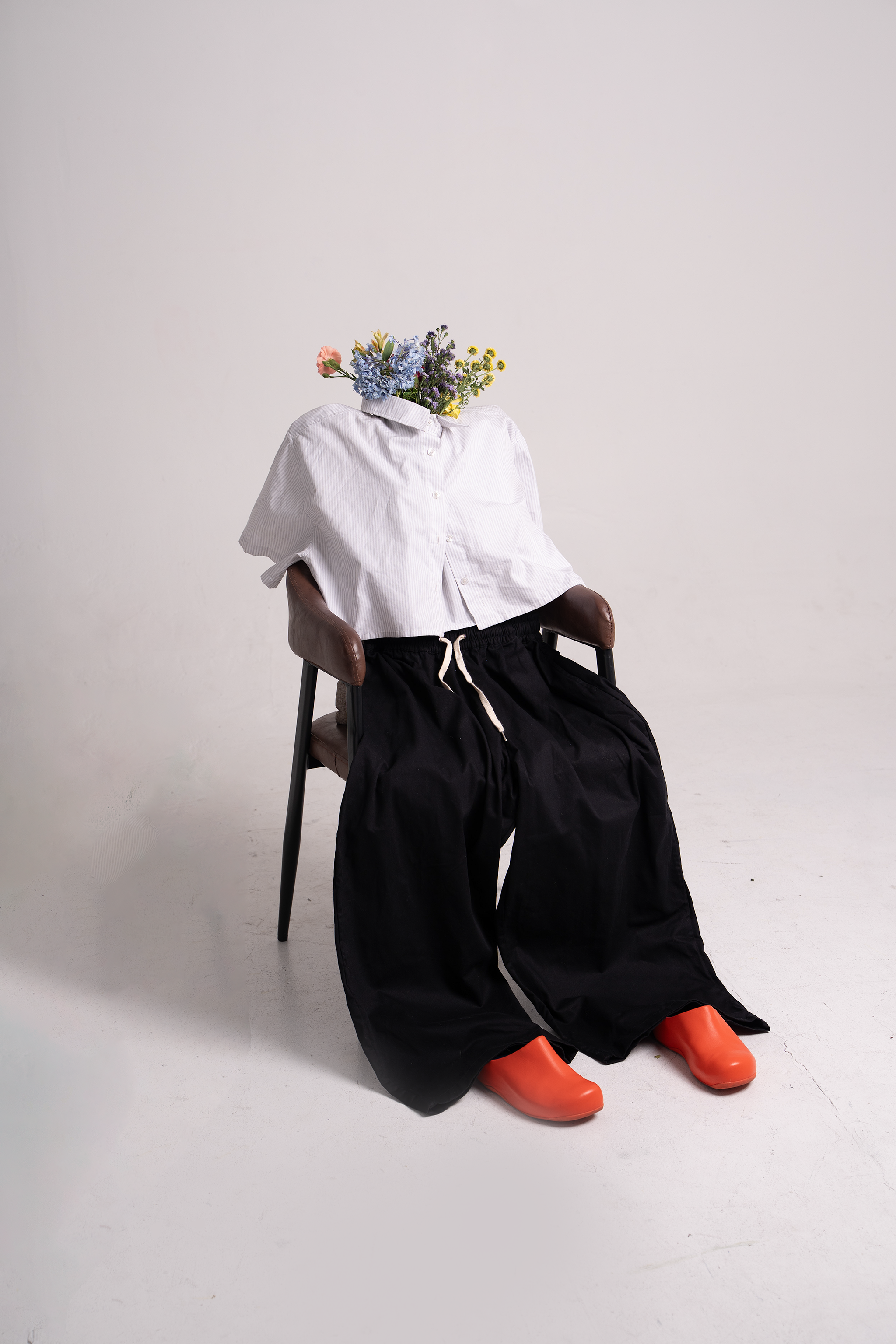 A white shirt, black pants, and orange shoes posed on a chair with flowers in the collar.