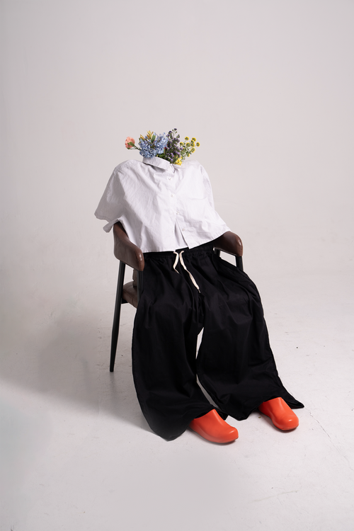 A white shirt, black pants, and orange shoes posed on a chair with flowers in the collar.