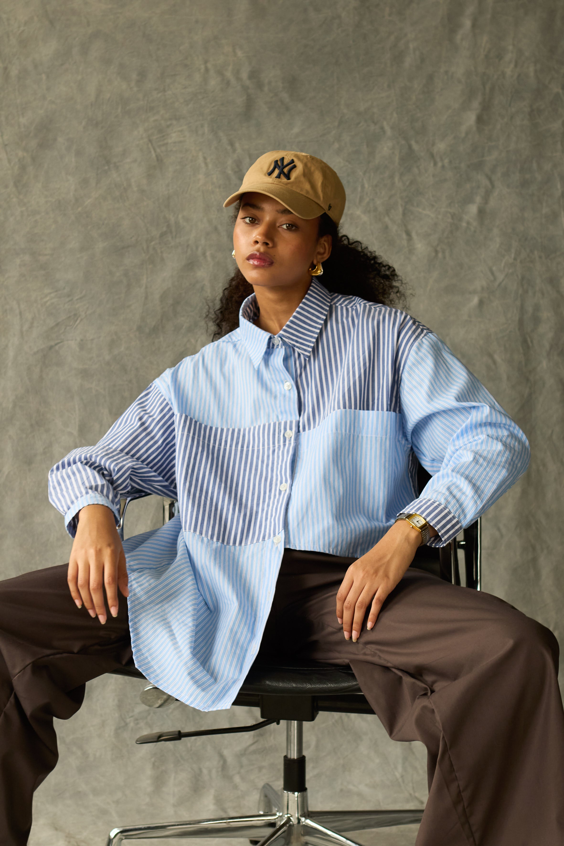 Person wearing a light blue shirt and brown cap sitting on a chair against a olive background
